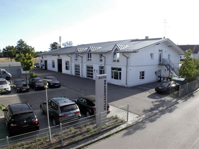 Autohaus- oder Werkstattgebäude mit mehreren geparkten Fahrzeugen auf dem Hof